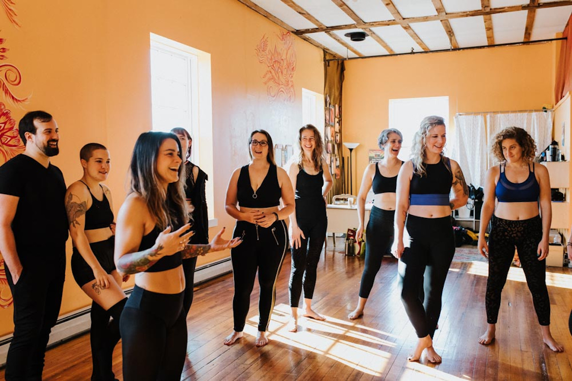 A group from a fitness class engaged in a lively conversation with their instructor at Hustle and Flow. The group includes both men and women, all wearing workout attire, with smiles and expressions of enjoyment as they participate in the class.