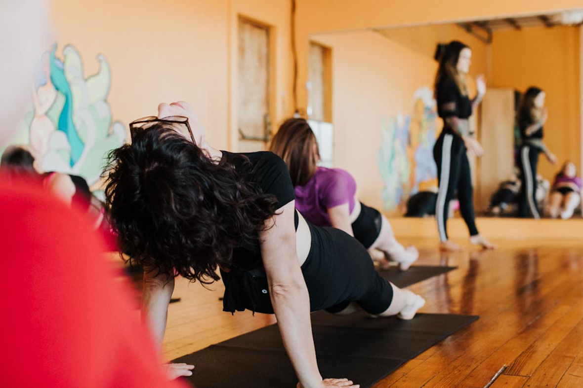 Participants in a yoga class at Hustle and Flow in Portland, Maine, engage in a side plank pose. The instructor, seen in the background, offers guidance and support.