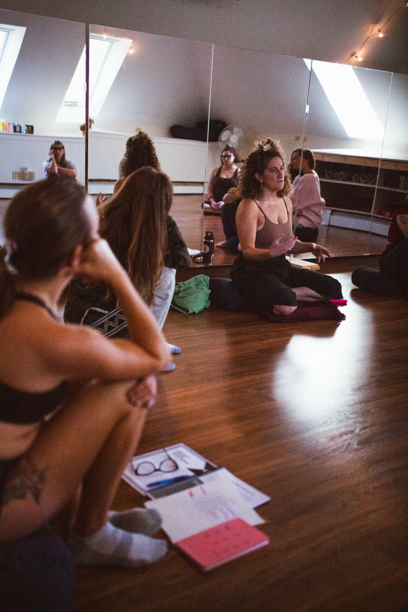 A group of women dressed in black shorts, fishnet stockings, and knee pads face the wall, posing in front of a colorful mural, showcasing their high heels. The photo only shows the women from the waist down.